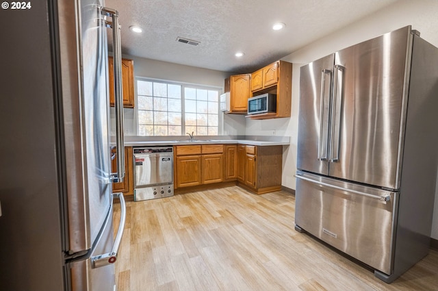 kitchen featuring a textured ceiling, light wood-type flooring, and appliances with stainless steel finishes