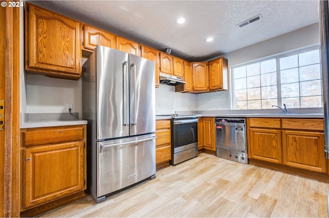 kitchen featuring appliances with stainless steel finishes, a textured ceiling, sink, and light hardwood / wood-style flooring