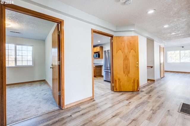 corridor with light hardwood / wood-style floors, plenty of natural light, and a textured ceiling