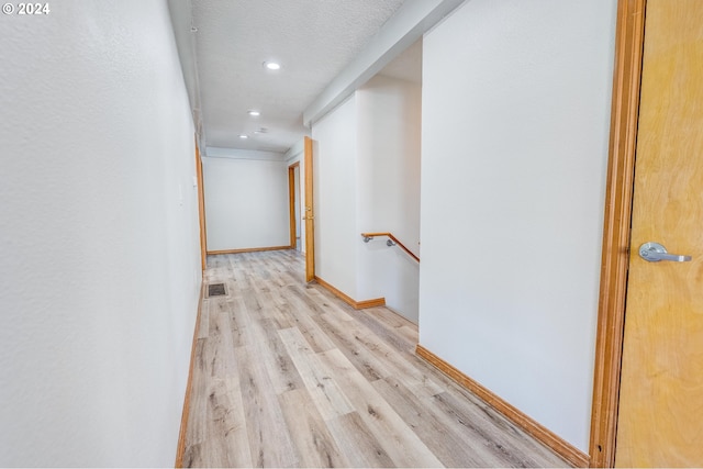 hallway with light wood-type flooring and a textured ceiling