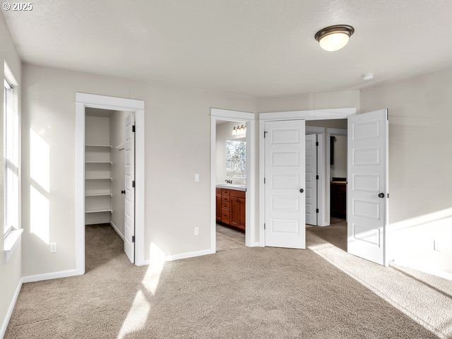 unfurnished bedroom with light carpet, ensuite bathroom, a closet, and a spacious closet