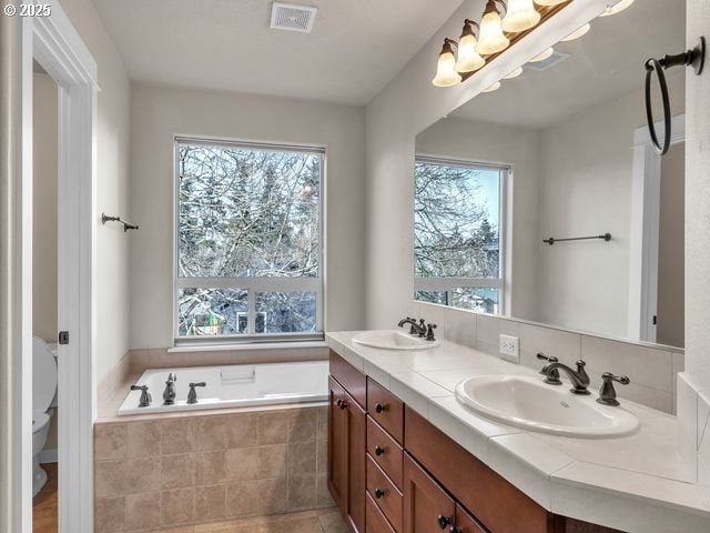 bathroom with toilet, tile patterned flooring, a relaxing tiled tub, and vanity