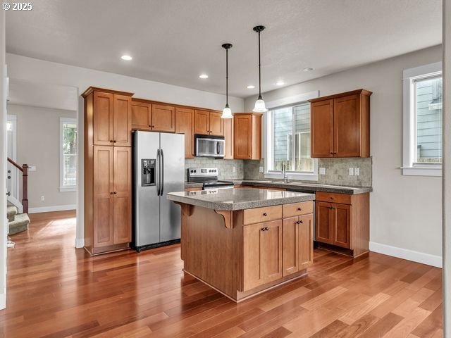 kitchen featuring a kitchen bar, hanging light fixtures, light wood-type flooring, a kitchen island, and stainless steel appliances