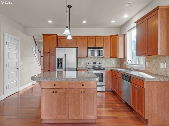 kitchen with a center island, sink, pendant lighting, backsplash, and stainless steel appliances