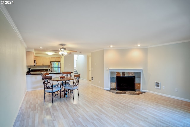 dining room with a tile fireplace, light wood-type flooring, ceiling fan, and ornamental molding