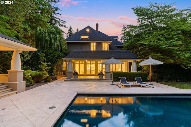 back house at dusk featuring a patio and an outbuilding