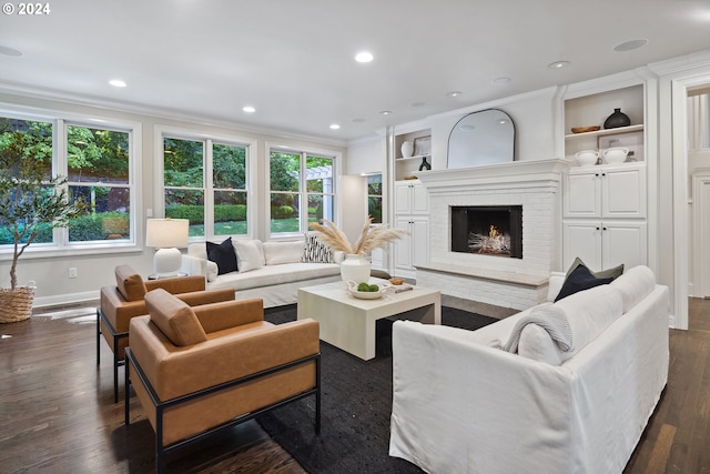 living room with built in features, dark wood-type flooring, a brick fireplace, and ornamental molding