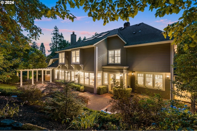 back house at dusk featuring a sunroom and a patio