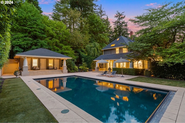 pool at dusk with an outbuilding, a patio area, and a yard