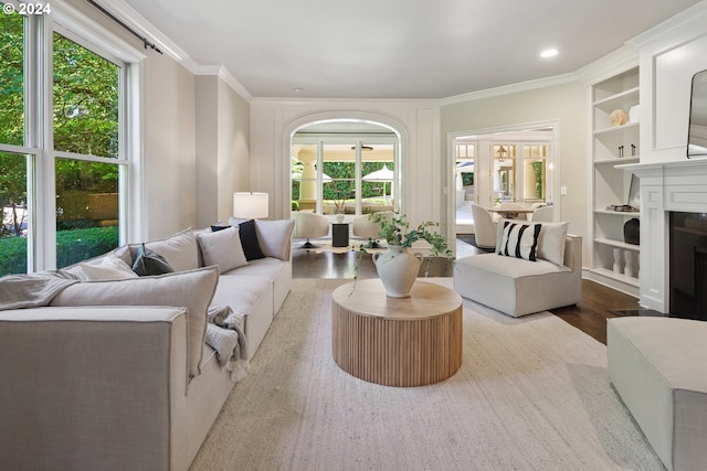 living room featuring built in features, crown molding, wood-type flooring, and a wealth of natural light