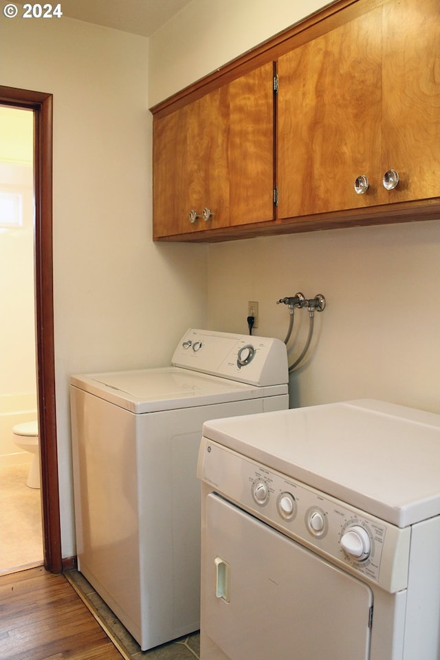 clothes washing area featuring cabinets, washing machine and clothes dryer, and light hardwood / wood-style flooring