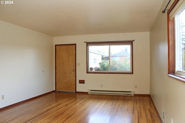 empty room with baseboard heating, plenty of natural light, a textured ceiling, and light wood-type flooring