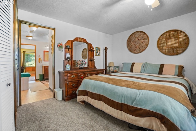 bedroom featuring ceiling fan, light colored carpet, a textured ceiling, and ensuite bath