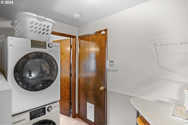 clothes washing area with stacked washer / drying machine, light tile patterned floors, and a textured ceiling