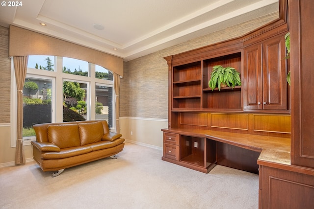 living area featuring light carpet, baseboards, wainscoting, a tray ceiling, and built in desk