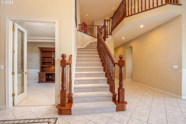 staircase featuring arched walkways, a high ceiling, tile patterned flooring, and baseboards