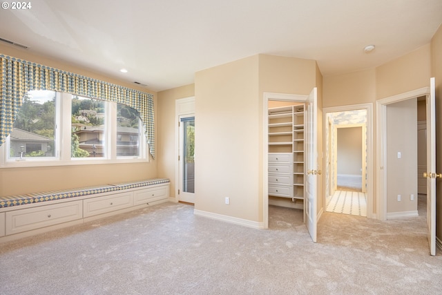 unfurnished bedroom with light carpet, a walk in closet, visible vents, and baseboards