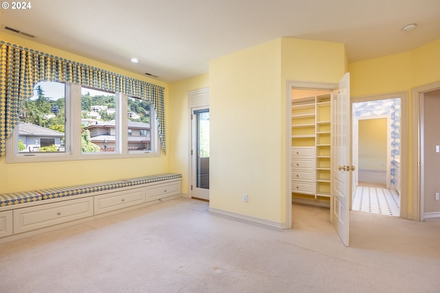 unfurnished bedroom with a walk in closet, recessed lighting, light colored carpet, visible vents, and baseboards