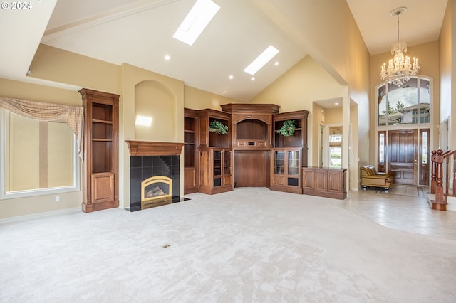 living area with a skylight, a tiled fireplace, carpet, high vaulted ceiling, and a notable chandelier