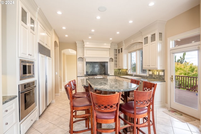 kitchen with built in appliances, a sink, a kitchen island, dark stone counters, and tasteful backsplash