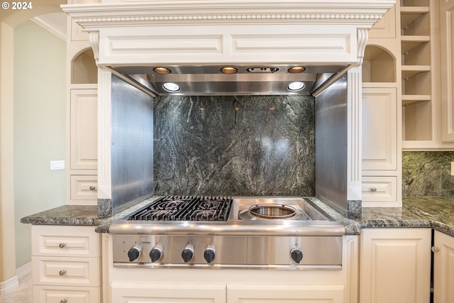 kitchen featuring arched walkways, dark stone countertops, backsplash, and stainless steel gas stovetop