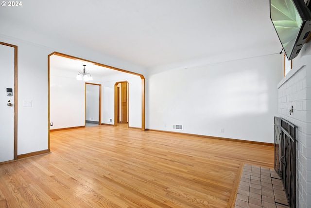 unfurnished living room with light hardwood / wood-style flooring, a notable chandelier, and a fireplace