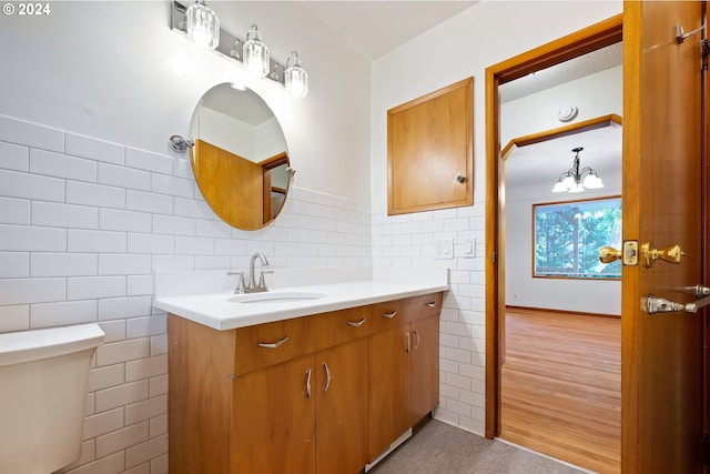 bathroom featuring toilet, wood-type flooring, vanity, a notable chandelier, and tile walls