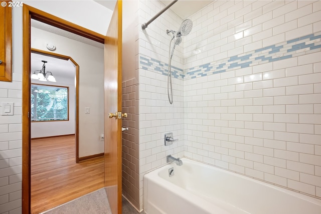 bathroom with an inviting chandelier, tiled shower / bath combo, and wood-type flooring