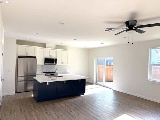 kitchen with white cabinets, tasteful backsplash, light hardwood / wood-style floors, an island with sink, and appliances with stainless steel finishes