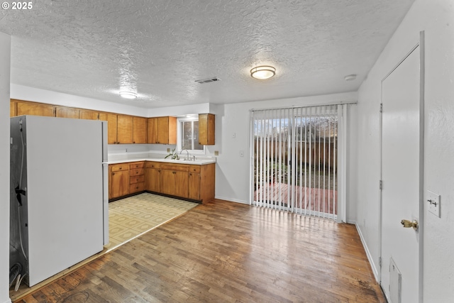 kitchen featuring a textured ceiling, white fridge, light hardwood / wood-style flooring, and sink