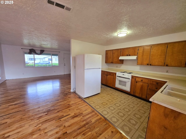 kitchen with light countertops, freestanding refrigerator, a sink, oven, and under cabinet range hood