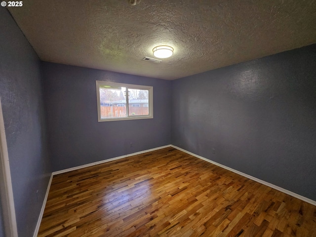 spare room featuring baseboards, a textured ceiling, visible vents, and wood finished floors