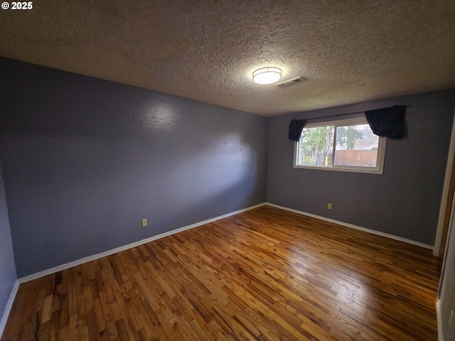 spare room with a textured ceiling, wood finished floors, visible vents, and baseboards