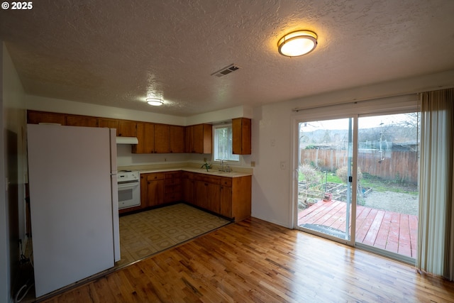 kitchen featuring light countertops, freestanding refrigerator, light wood-type flooring, range, and under cabinet range hood