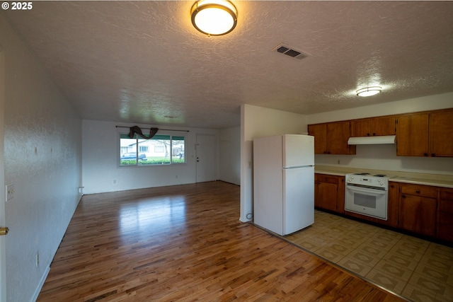 kitchen featuring white appliances, visible vents, brown cabinets, light countertops, and under cabinet range hood