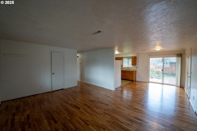 unfurnished living room with light wood-type flooring, a sink, visible vents, and a textured ceiling