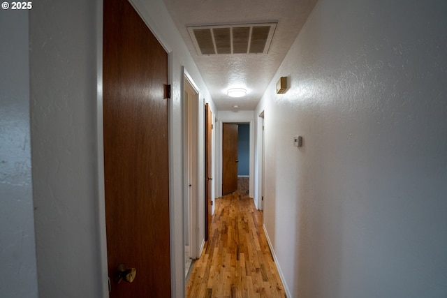 hall with a textured ceiling, a textured wall, light wood finished floors, and visible vents