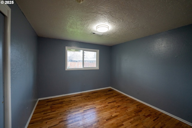 spare room with visible vents, a textured ceiling, baseboards, and wood finished floors