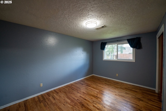 empty room featuring wood finished floors, visible vents, and baseboards