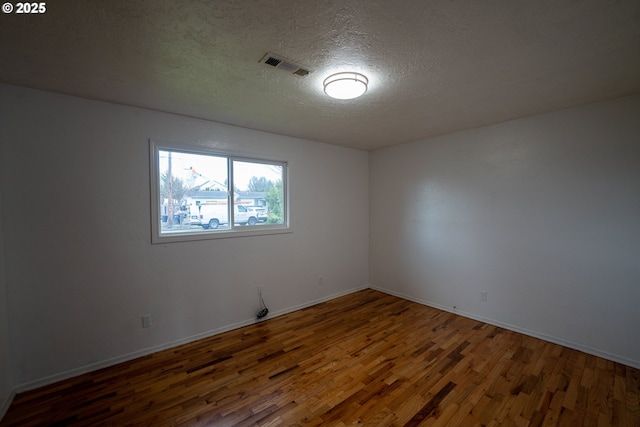 spare room featuring dark wood-style floors, visible vents, a textured ceiling, and baseboards