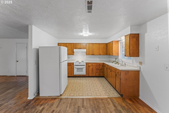 kitchen with stove, light wood-type flooring, a textured ceiling, sink, and white fridge