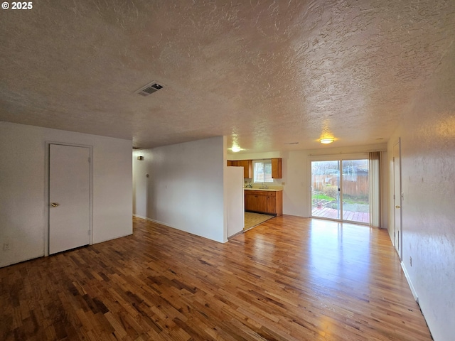 unfurnished living room with a textured ceiling, visible vents, and light wood-style floors