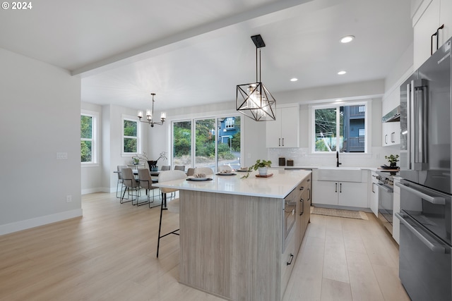 kitchen with premium appliances, light wood-type flooring, a kitchen island, decorative light fixtures, and white cabinetry