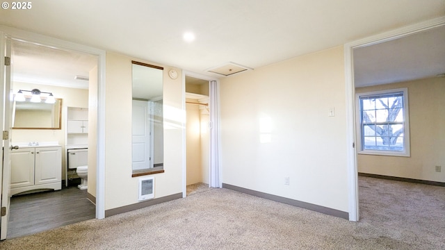 unfurnished bedroom featuring heating unit, light carpet, and ensuite bath