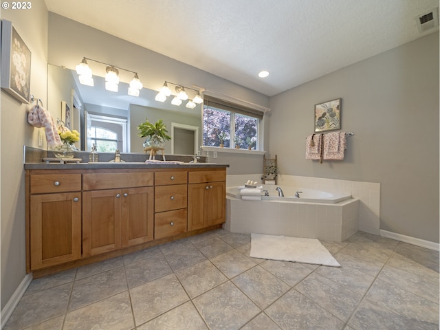 bathroom featuring tiled tub, tile patterned floors, vanity, and a textured ceiling