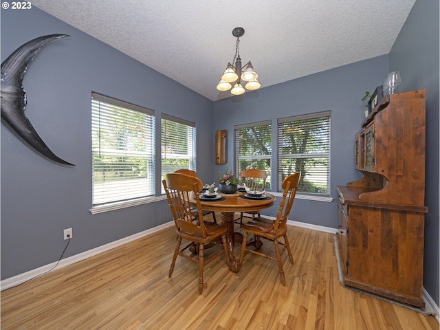 dining area with a textured ceiling, light hardwood / wood-style flooring, and an inviting chandelier