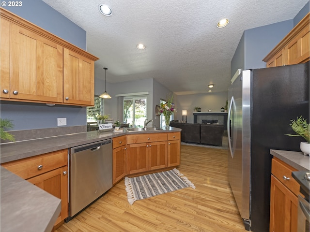 kitchen featuring appliances with stainless steel finishes, decorative light fixtures, a textured ceiling, light hardwood / wood-style flooring, and sink