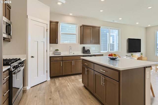 kitchen featuring appliances with stainless steel finishes, light wood-type flooring, a kitchen island, and sink