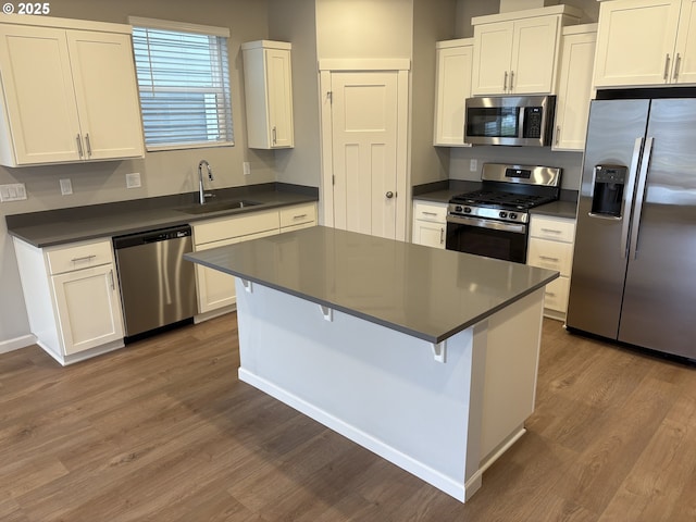 kitchen with dark countertops, wood finished floors, stainless steel appliances, and a sink