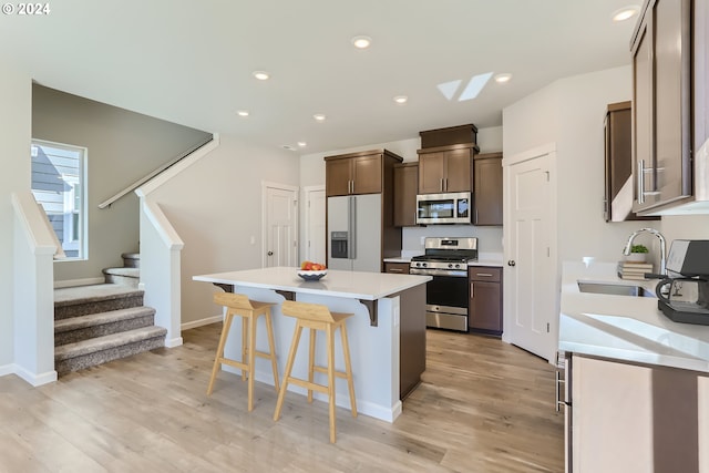 kitchen featuring a kitchen island, a breakfast bar, stainless steel appliances, light wood-style floors, and a sink